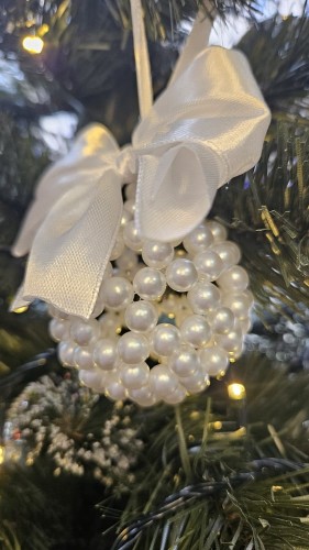 Ręcznie wykonana biała bombka z akrylowych koralików, ozdobiona elegancką białą kokardą, zawieszona na choince – świąteczna dekoracja handmade.
